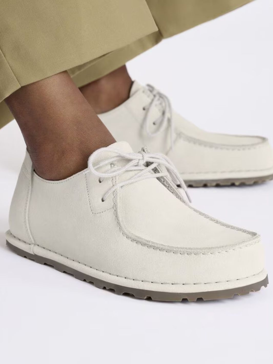Bilde av føtter med hvite semskede sko fra Birkenstock. Bilde er tatt i studio med hvit bakgrunn.