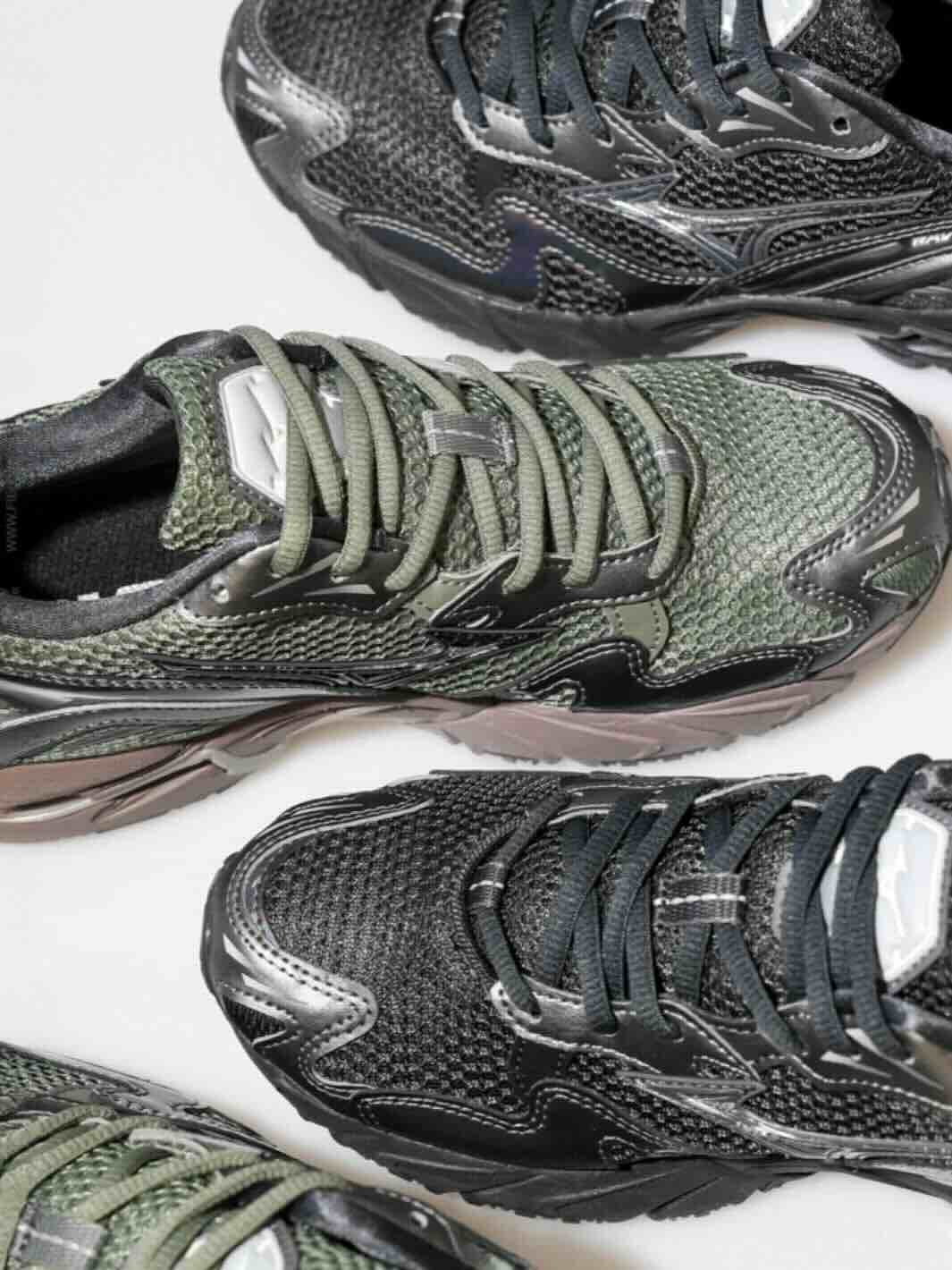 Bilde tatt i studio på hvit bakgrunn ovenfra av svarte og mørkegrønne joggesko fra merket Mizuo. 